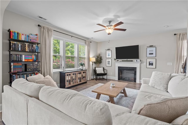 living room featuring ceiling fan, wood finished floors, baseboards, and a glass covered fireplace