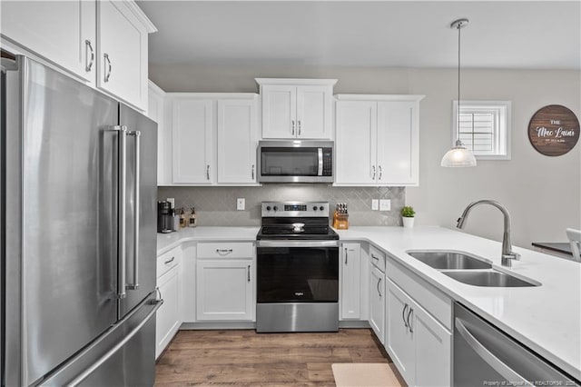 kitchen featuring stainless steel appliances, a sink, white cabinetry, tasteful backsplash, and wood finished floors