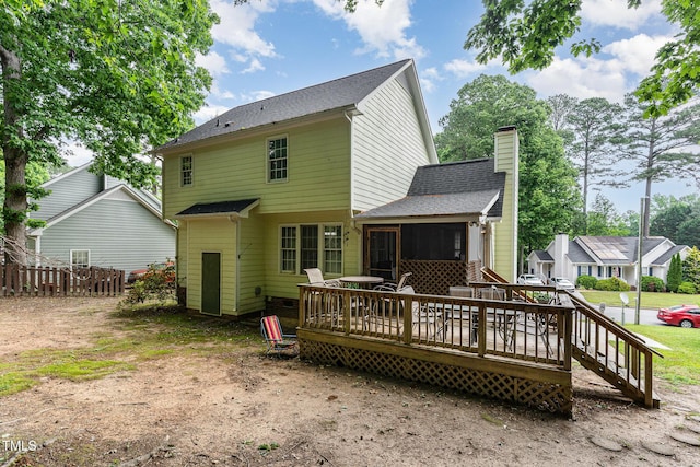 back of property with a chimney, a wooden deck, fence, a sunroom, and a shingled roof