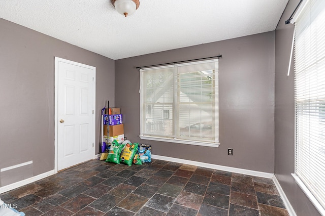 rec room with baseboards, stone tile flooring, and a textured ceiling