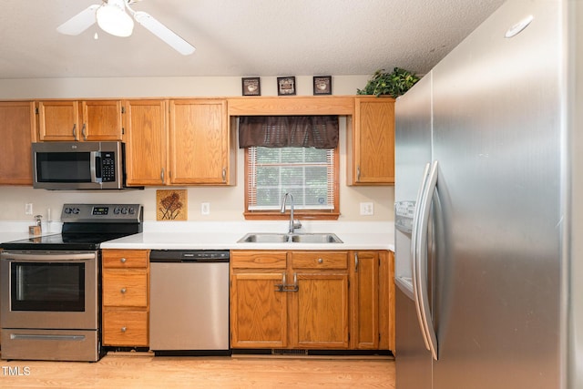 kitchen featuring stainless steel appliances, a sink, light countertops, light wood-style floors, and a textured ceiling