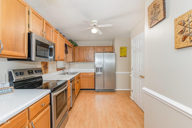 kitchen with appliances with stainless steel finishes, a sink, light wood finished floors, ceiling fan, and light countertops