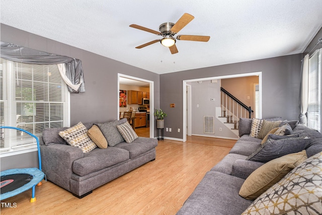 living area featuring light wood-style flooring, a ceiling fan, stairway, and a textured ceiling