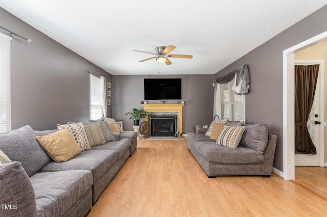 living room with light wood-style floors, a ceiling fan, a premium fireplace, and baseboards