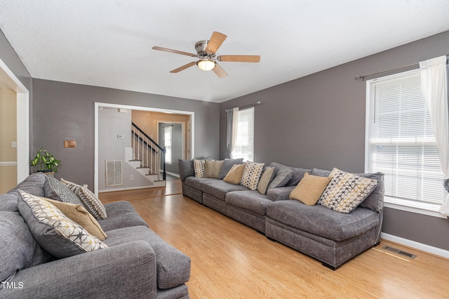living area featuring stairs, light wood finished floors, ceiling fan, and baseboards