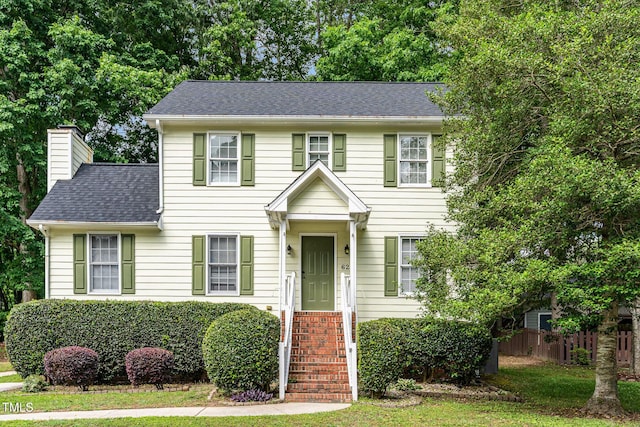 colonial-style house with fence, a chimney, and a shingled roof