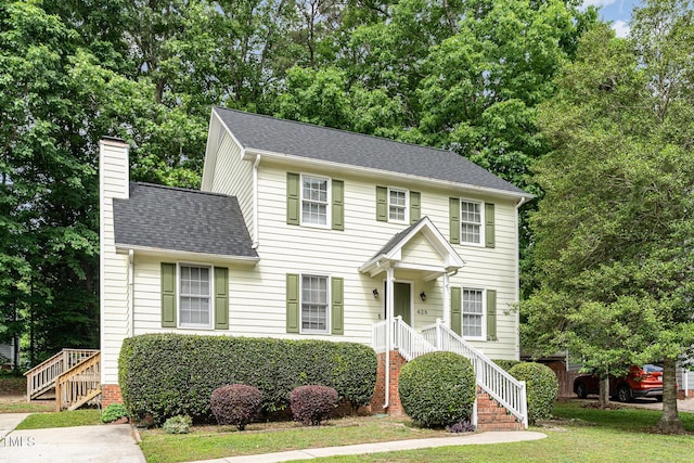 colonial house featuring a chimney, a front lawn, and a shingled roof