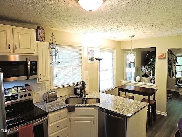 8 Woodsprite Ct, Durham, NC 27703 - kitchen with stainless steel appliances, a sink, a textured ceiling, stone counters, and dark wood finished floors