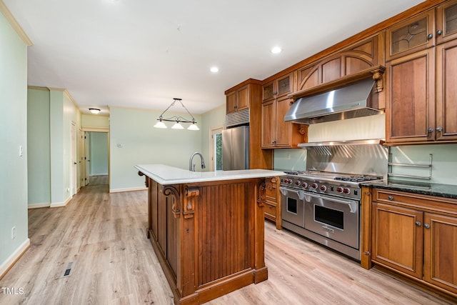 kitchen featuring appliances with stainless steel finishes, exhaust hood, light wood finished floors, brown cabinetry, and recessed lighting