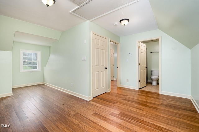 unfurnished bedroom with attic access, light wood-style flooring, baseboards, and connected bathroom