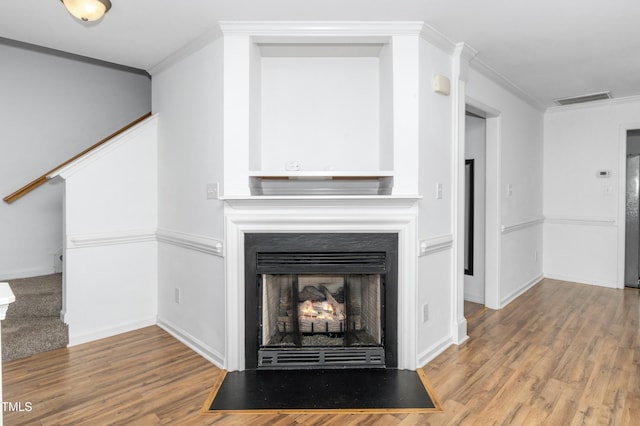 unfurnished living room featuring crown molding, wood finished floors, baseboards, stairs, and a fireplace with flush hearth