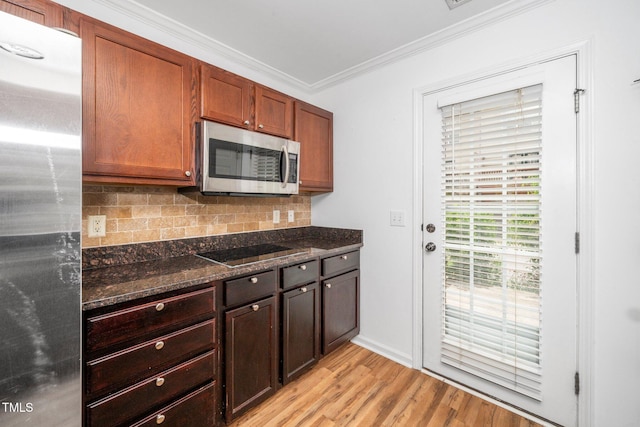 kitchen with stainless steel appliances, crown molding, dark stone countertops, backsplash, and light wood-type flooring