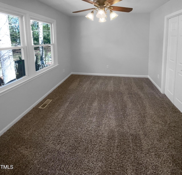 unfurnished room with a ceiling fan, dark colored carpet, and baseboards