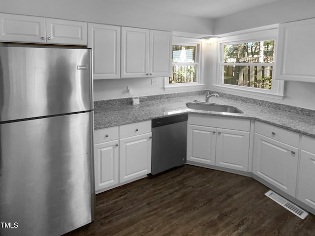 kitchen with stainless steel appliances, a sink, white cabinets, dark wood-type flooring, and light stone countertops