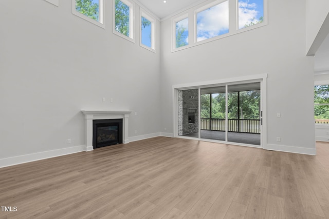 248 Ashford Dr, Pittsboro, NC 27312 - unfurnished living room featuring a glass covered fireplace, a towering ceiling, baseboards, and light wood-style floors