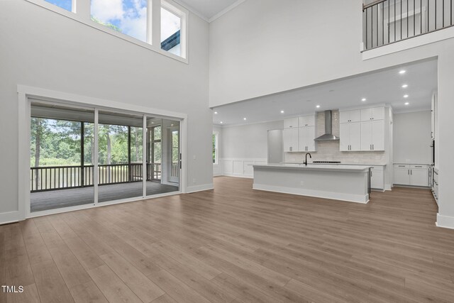 248 Ashford Dr, Pittsboro, NC 27312 - unfurnished living room featuring crown molding, light wood-style flooring, a towering ceiling, baseboards, and a sink