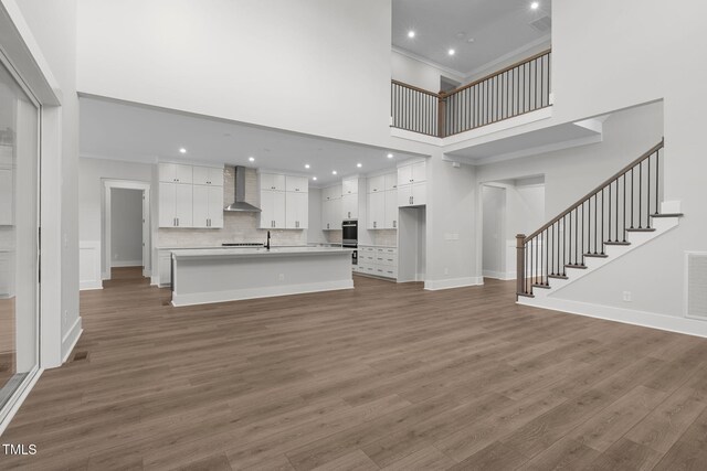 248 Ashford Dr, Pittsboro, NC 27312 - unfurnished living room featuring a towering ceiling, wood finished floors, stairs, baseboards, and recessed lighting