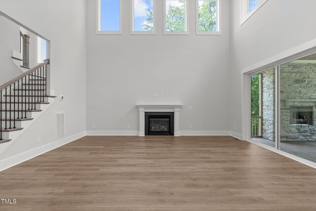 248 Ashford Dr, Pittsboro, NC 27312 - unfurnished living room with a fireplace, a towering ceiling, plenty of natural light, and light wood-style floors