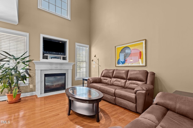living room with wood finished floors, plenty of natural light, a fireplace with flush hearth, and a high ceiling