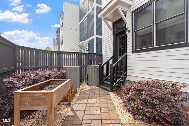 view of patio / terrace with central AC unit, entry steps, fence, and a vegetable garden