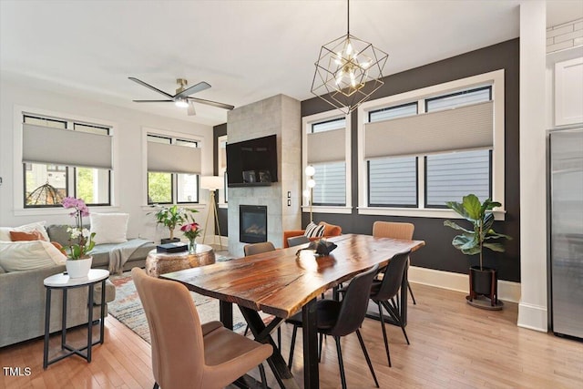 dining area featuring a tile fireplace, light wood-style flooring, baseboards, and a chandelier