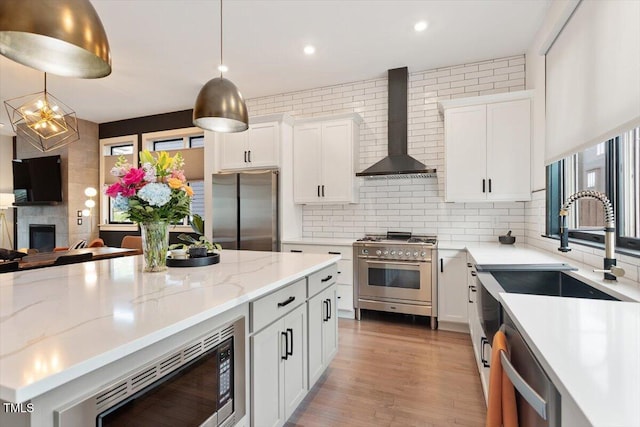 kitchen with appliances with stainless steel finishes, wall chimney exhaust hood, decorative backsplash, white cabinets, and recessed lighting