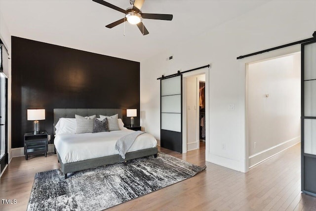 bedroom featuring a barn door, wood finished floors, a spacious closet, and baseboards