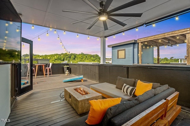 deck at dusk with a ceiling fan and an outdoor living space with a fire pit