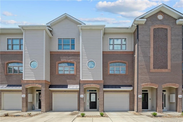 multi unit property featuring driveway, brick siding, a garage, and a standing seam roof