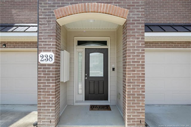 doorway to property featuring brick siding, a garage, and a standing seam roof