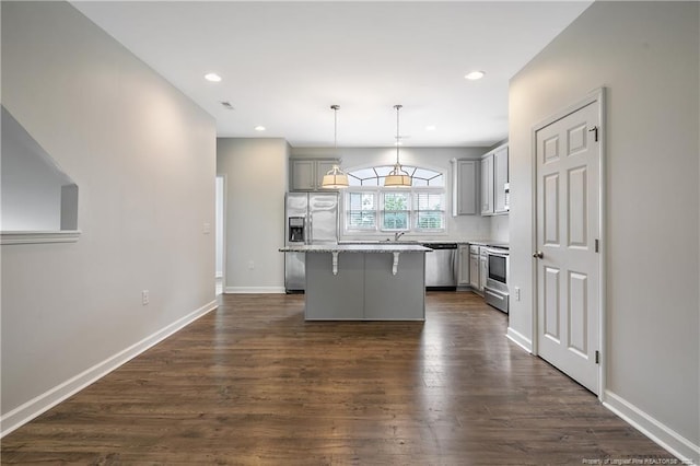 kitchen with stainless steel appliances, gray cabinets, a kitchen breakfast bar, a kitchen island, and dark wood-type flooring