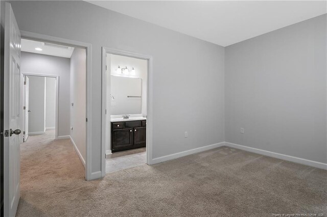 unfurnished bedroom featuring light carpet, baseboards, a sink, and ensuite bath