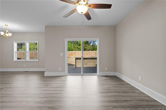 unfurnished room with healthy amount of natural light, a chandelier, wood finished floors, and ceiling fan