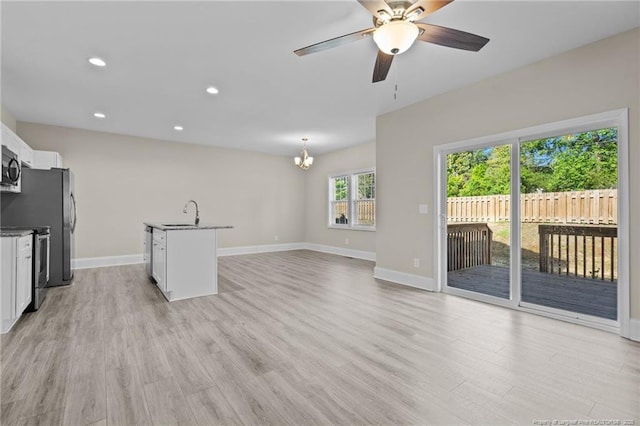 unfurnished living room featuring a chandelier, light wood-type flooring, baseboards, a ceiling fan, and recessed lighting