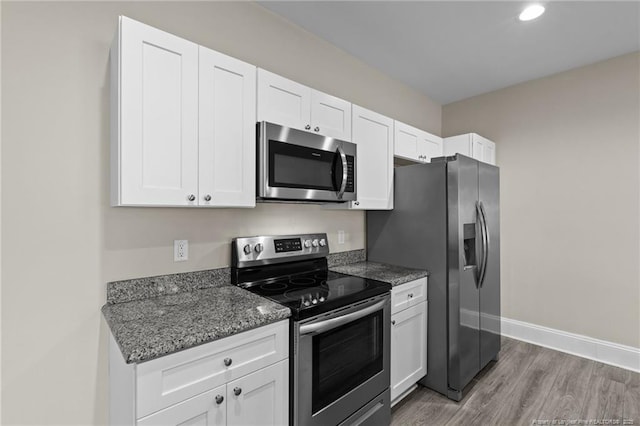 kitchen with appliances with stainless steel finishes, light wood-type flooring, white cabinetry, baseboards, and dark stone counters