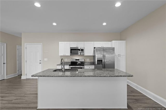kitchen with stainless steel appliances, a sink, white cabinetry, dark wood-style flooring, and dark stone countertops