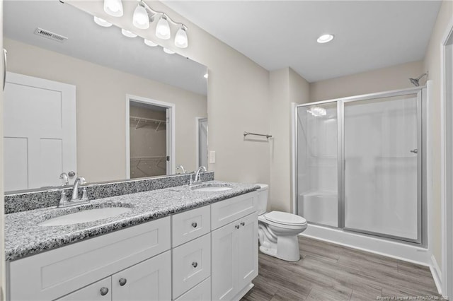 full bath featuring a stall shower, double vanity, toilet, wood finished floors, and recessed lighting