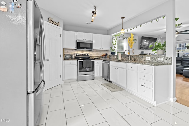 kitchen with stainless steel appliances, a sink, white cabinetry, dark stone counters, and tasteful backsplash
