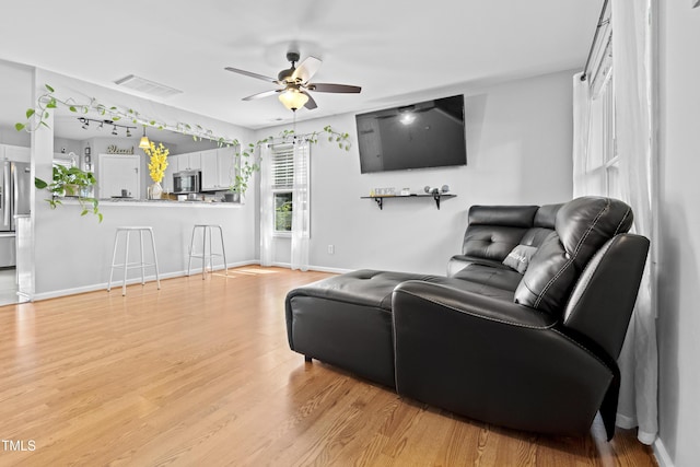 living area featuring a ceiling fan, light wood-style flooring, and baseboards