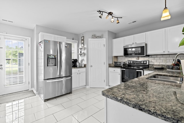 kitchen featuring appliances with stainless steel finishes, a sink, dark stone countertops, and white cabinetry
