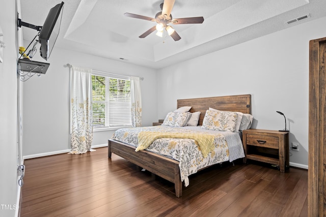bedroom featuring a raised ceiling, wood finished floors, baseboards, and a ceiling fan