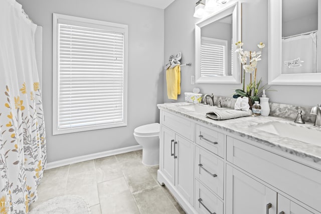 full bath featuring toilet, double vanity, baseboards, and plenty of natural light