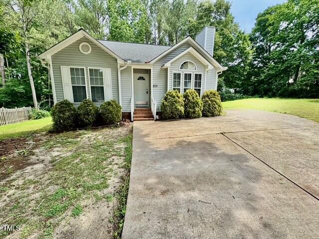 view of front of house with a chimney, view of wooded area, and fence