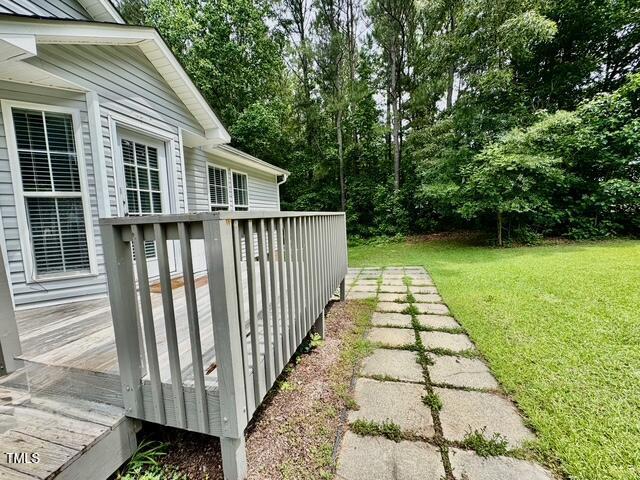 view of grassy yard with a wooden deck and view of scattered trees