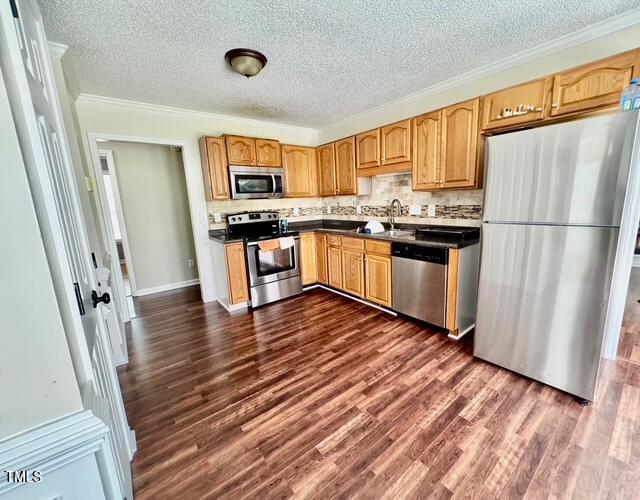 kitchen with stainless steel appliances, a textured ceiling, dark wood-style floors, crown molding, and backsplash