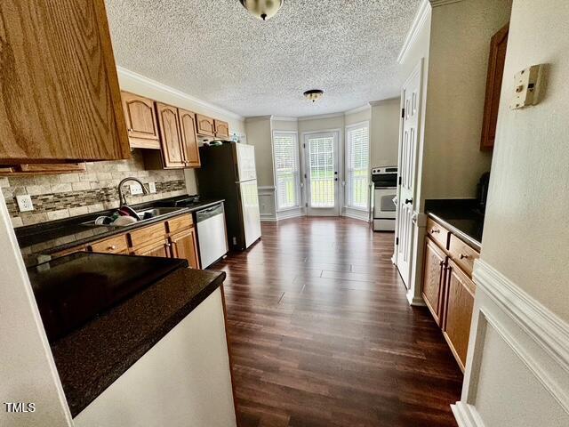 kitchen featuring appliances with stainless steel finishes, dark countertops, a sink, dark wood-type flooring, and decorative backsplash
