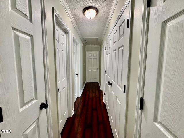 hall featuring a textured ceiling, attic access, dark wood-style floors, baseboards, and ornamental molding