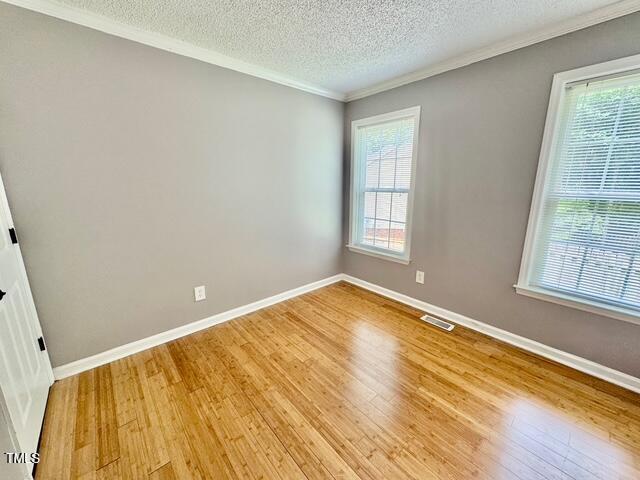 spare room featuring light wood-style floors, healthy amount of natural light, crown molding, a textured ceiling, and baseboards