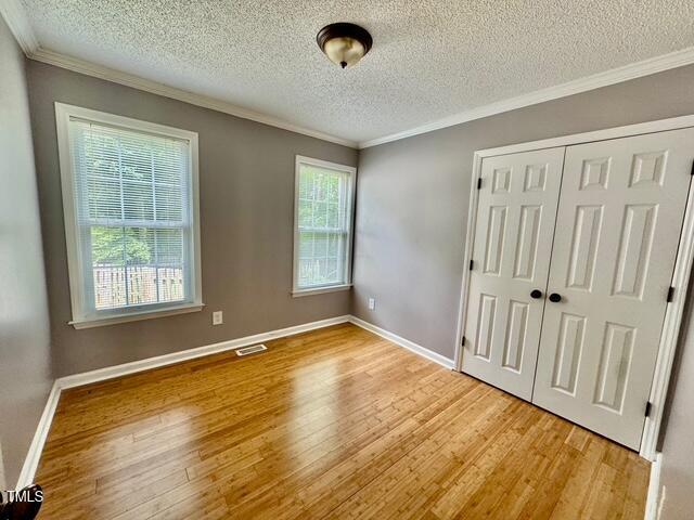 unfurnished bedroom featuring wood finished floors, a textured ceiling, crown molding, a closet, and baseboards
