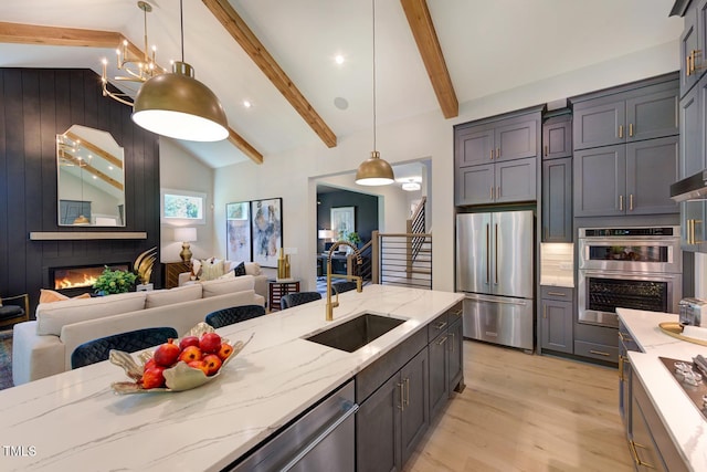 kitchen with appliances with stainless steel finishes, open floor plan, a sink, light stone countertops, and light wood finished floors